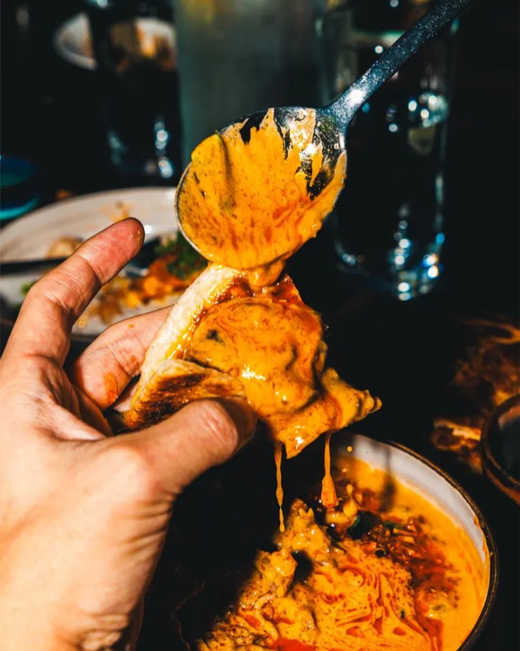 A hand dipping a folded tortilla into a bowl of mole, the sauce dripping from a spoon, at Darío's table.