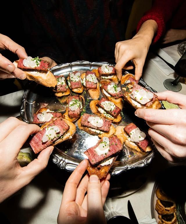 Several hands reaching into one tray of food.